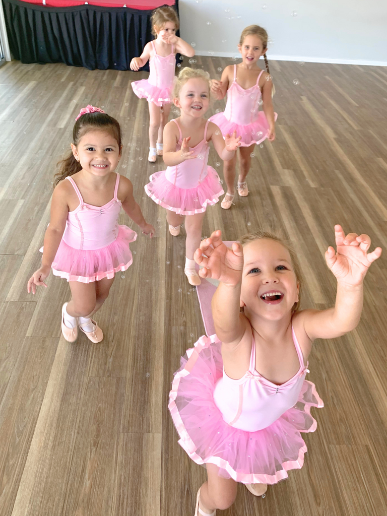 A group of ballerinas run around the studio in pink tutus laughing as they chase bubbles in a ballet class for 4 year olds.