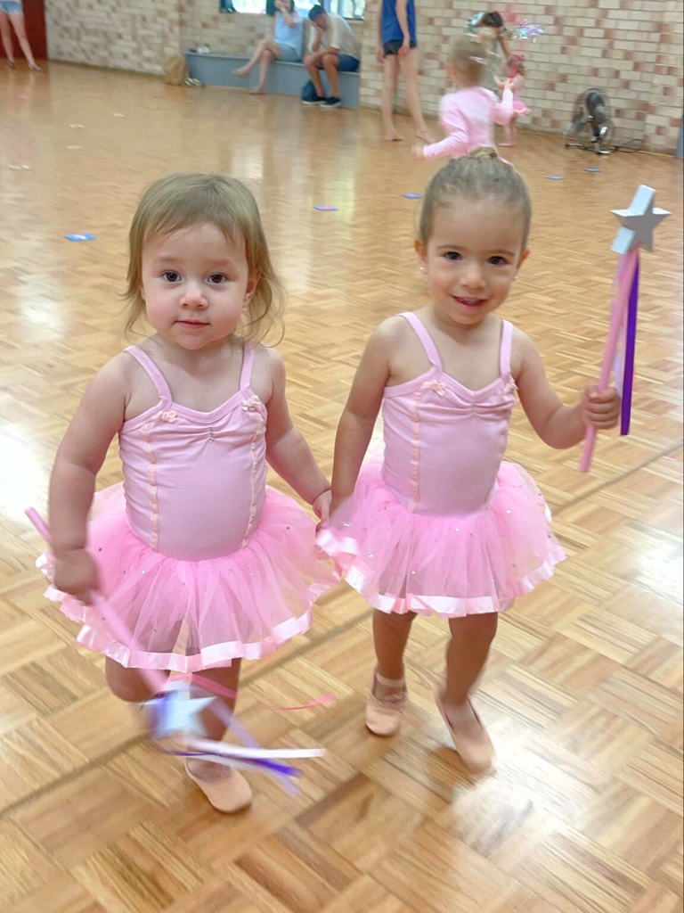 Two ballerinas in pink tutus pose with pink and purple fairy wands in a ballet class for 3 year olds. 