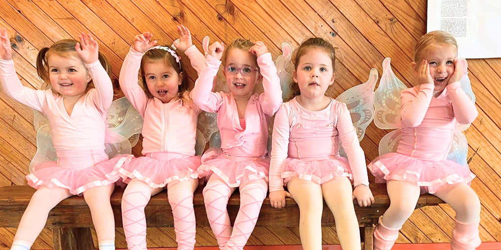 Five young girls in pink ballet outfits and fairy wings smiling and waving in a ballet class for 4 year olds in Newcastle.
