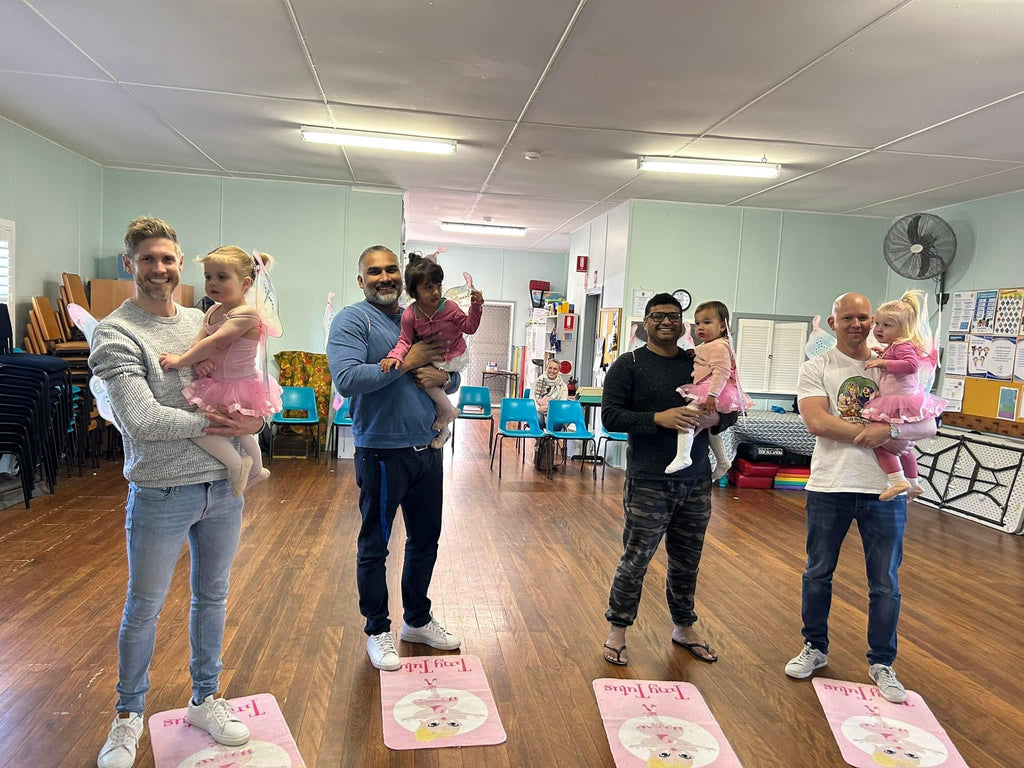 Four dads stand in a row holding their daughters in a rehearsal lesson for the Daddy Daughter Dance performance in Newcastle. 