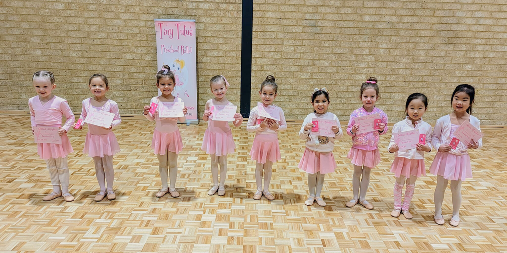 Tiny Tutus ballet class for 4 year old ballerinas standing in a row in pink tutus proudly showing off their certificates.  