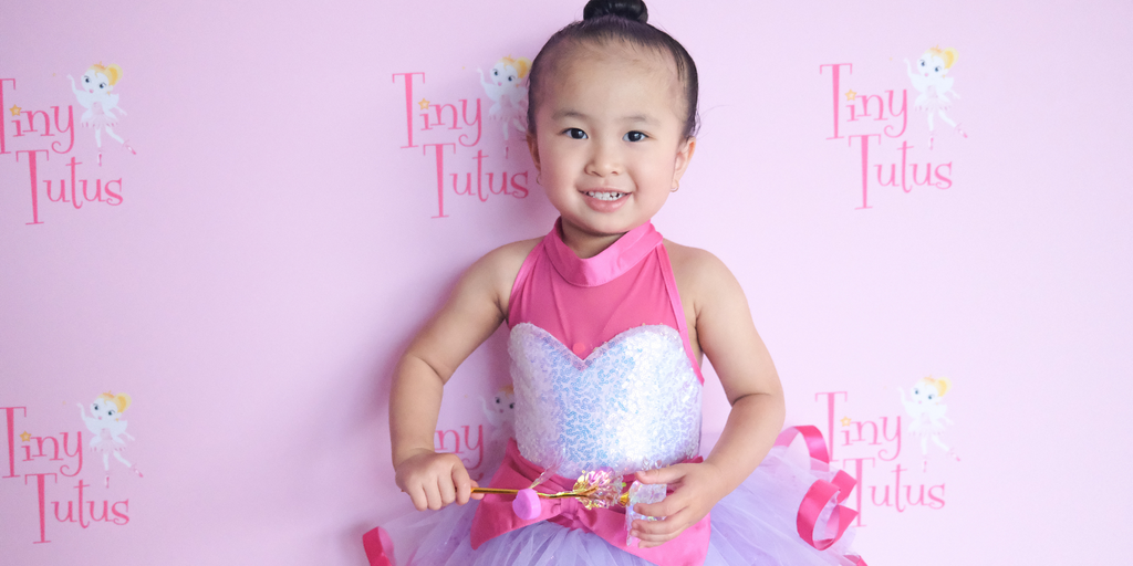 A 2 year old girl in a pink and purple tutu at a Tiny Tutus dance recital in Brisbane holding a light up flower. 