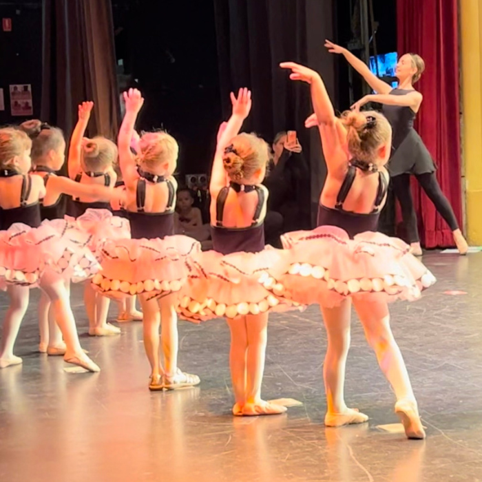 A group of ballerinas follow their teachers direction on the stage during a Tiny Tutus recital performance for ballet class for 4 year olds. 