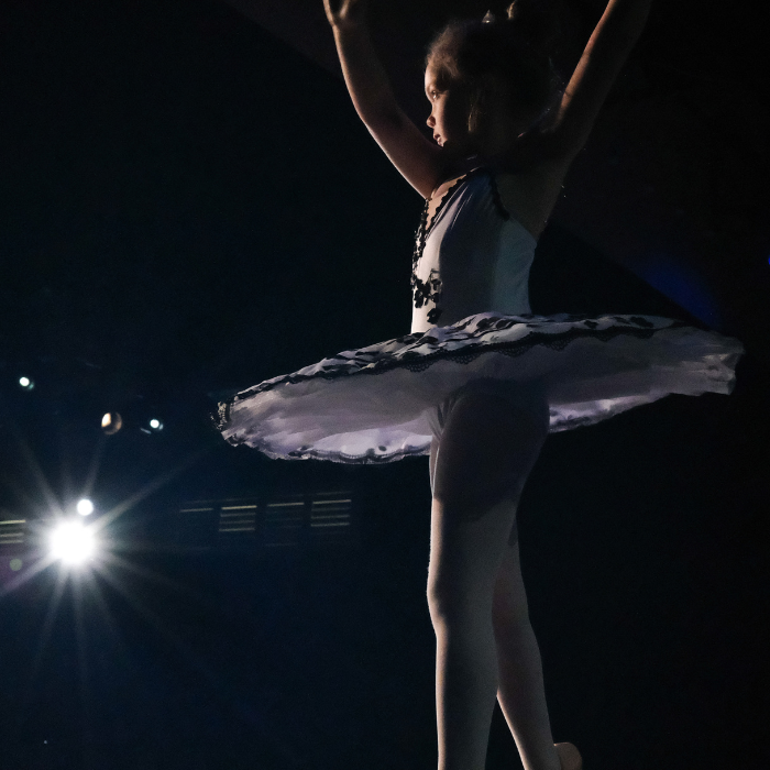A ballerina spins on stage in a black and white tutu with a spotlight in the background at the Newcastle. 